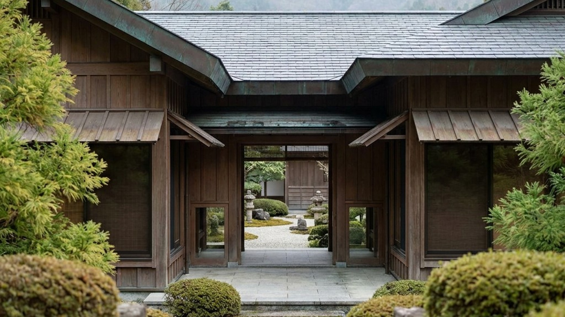 Symmetrical machiya façade opening onto a raked gravel garden, framed by karikomi shrubs and misty mountains